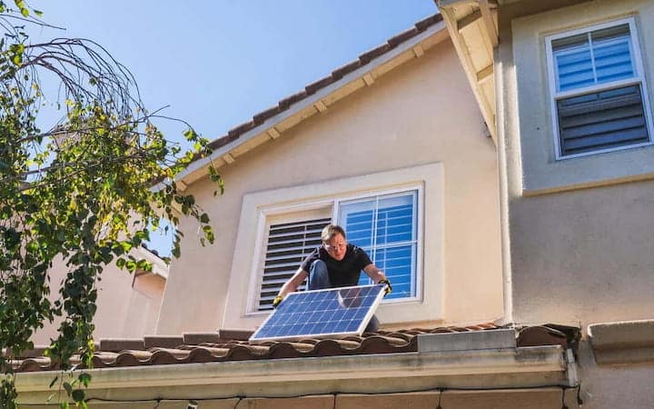 Artisan installe un panneau solaire sur le toit d'une maison