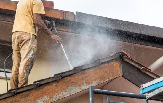 Travailleur utilisant un pistolet pulvérisateur à jet d'eau à haute pression avec un produit naturel pour laver et nettoyer la saleté des dalles de toit